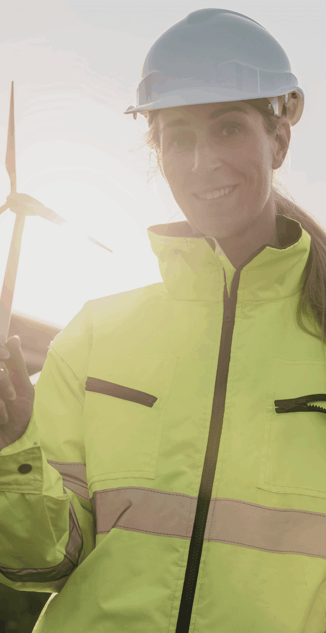 Female renewable energy professional in high-visibility gear holding a wind turbine model, standing beside solar panels - representing hiring challenges and solutions in the clean energy sector.
