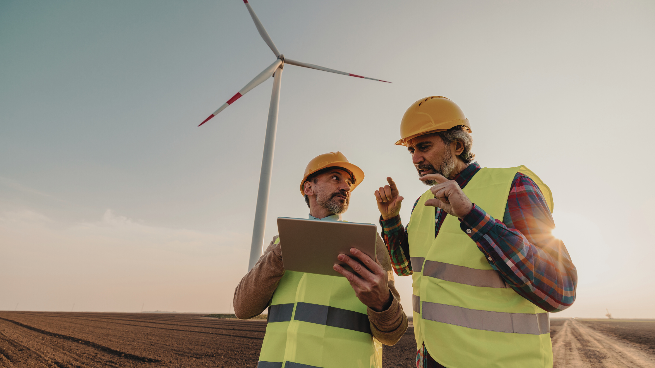 Two renewable energy professionals reviewing project plans during onboarding at a wind farm site