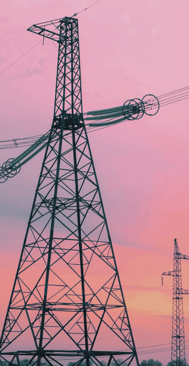 High-voltage transmission towers at sunset, representing the modernisation of grid infrastructure for renewable energy integration