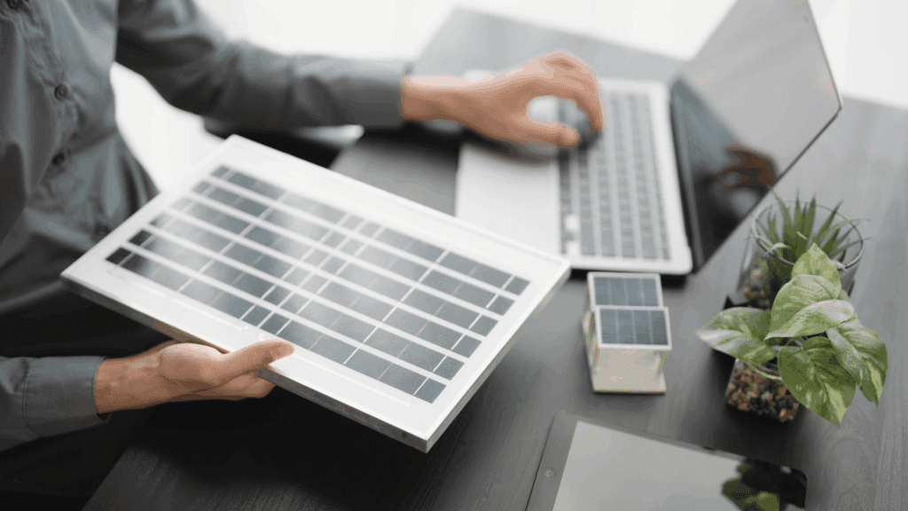 A renewable energy professional holding a solar panel while researching clean energy career opportunities on a laptop.