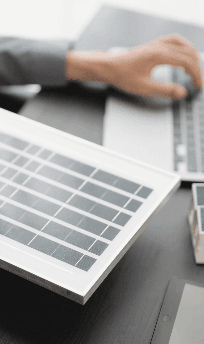 A renewable energy professional holding a solar panel while researching clean energy career opportunities on a laptop.