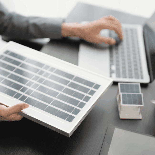 A renewable energy professional holding a solar panel while researching clean energy career opportunities on a laptop.