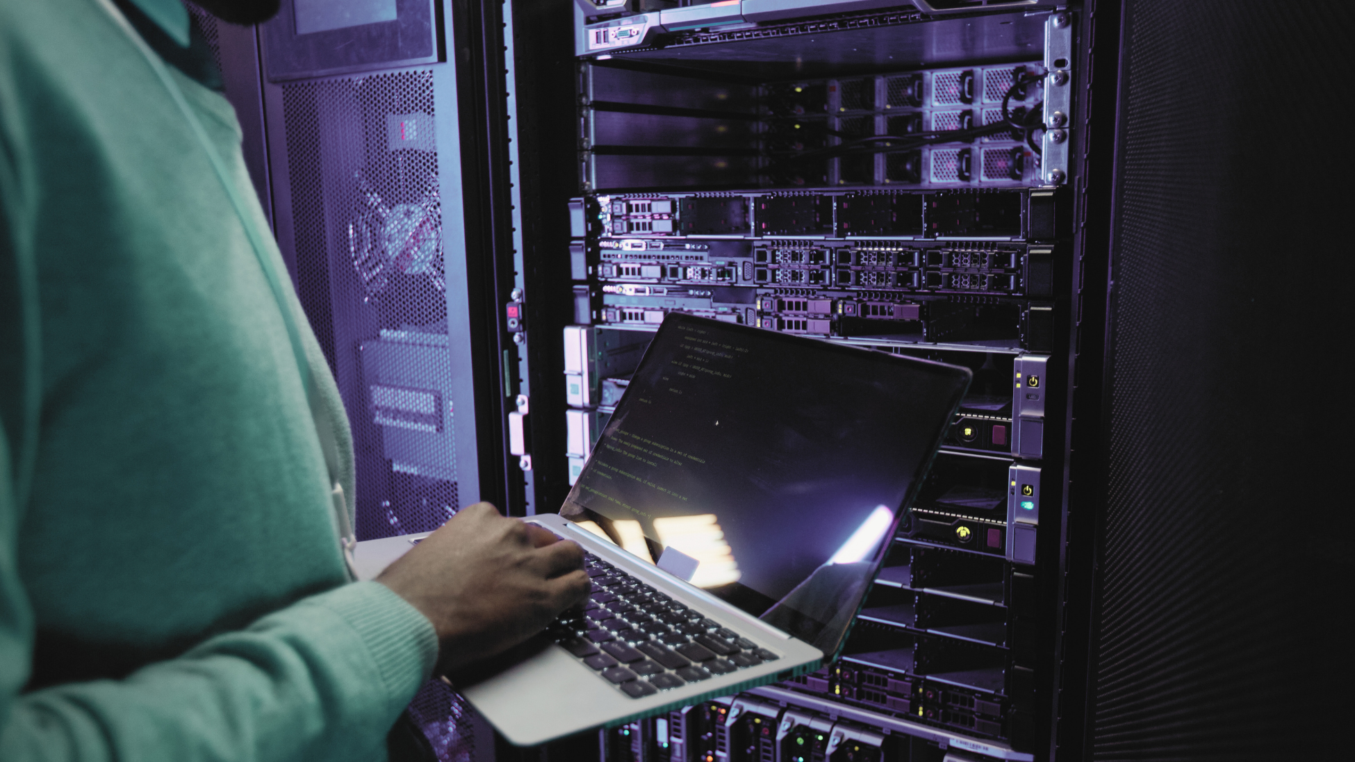An engineer working on a laptop in a data centre server room, maintaining energy and infrastructure systems.