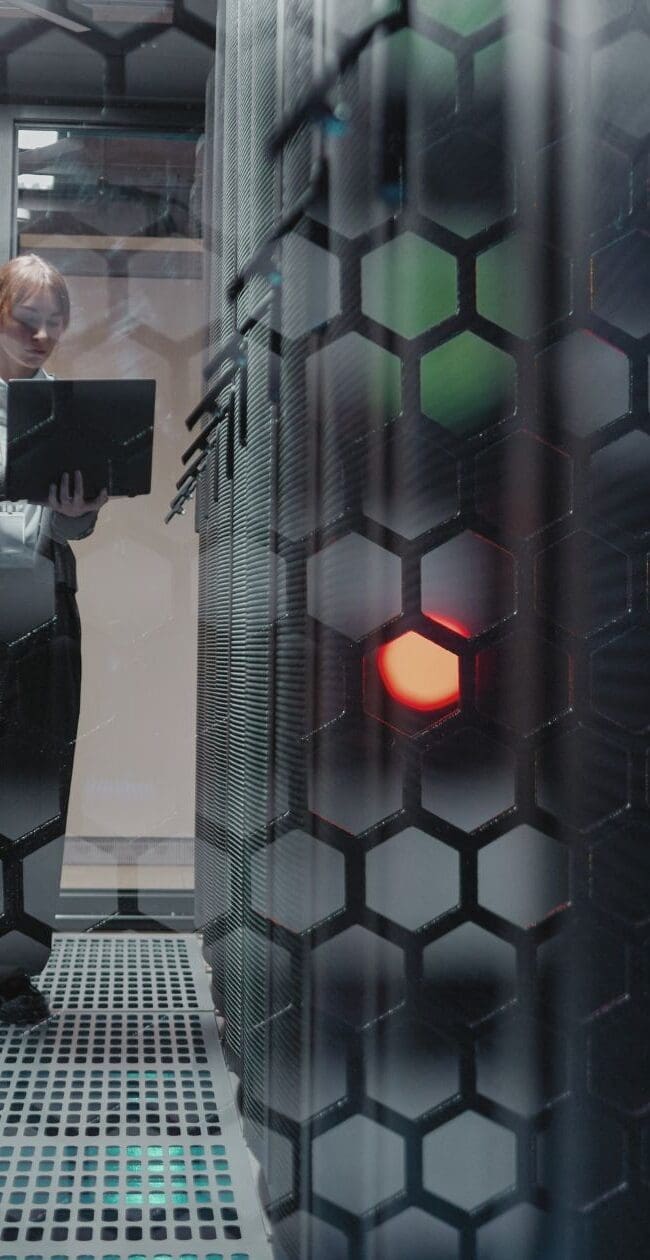 Engineer using a laptop inside a data centre server room, surrounded by racks and digital infrastructure equipment