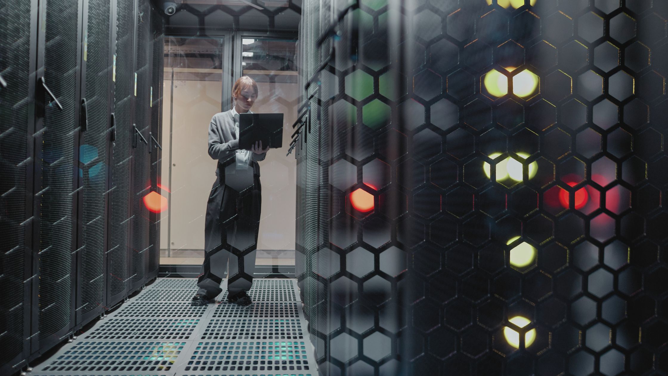 Engineer using a laptop inside a data centre server room, surrounded by racks and digital infrastructure equipment