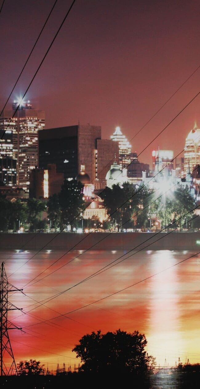 Electricity transmission towers and power lines near a city skyline at night, representing grid infrastructure and energy supply