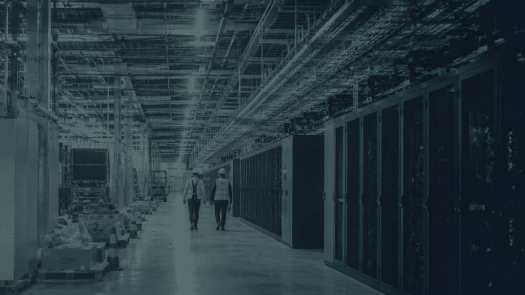 Two data centre professionals walking through a facility under construction, surrounded by server infrastructure and electrical systems.