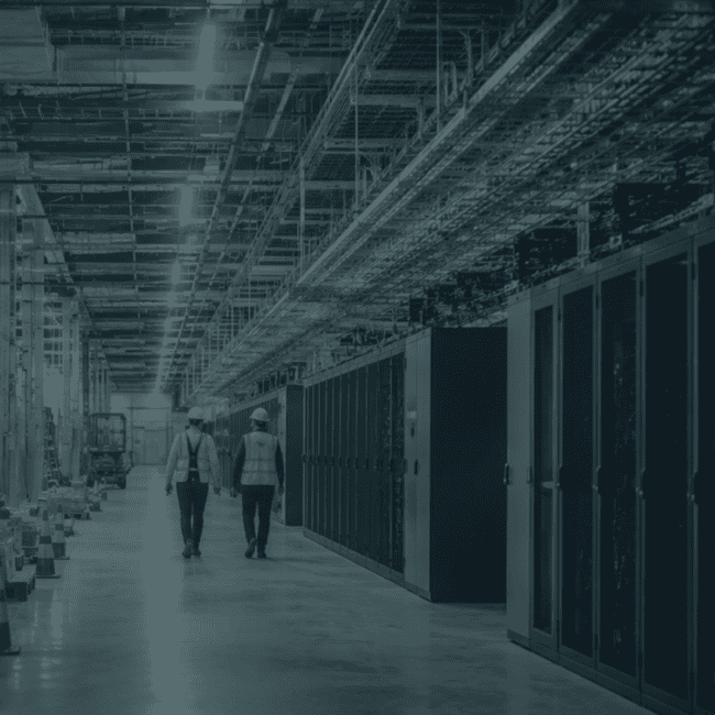 Two data centre professionals walking through a facility under construction, surrounded by server infrastructure and electrical systems.